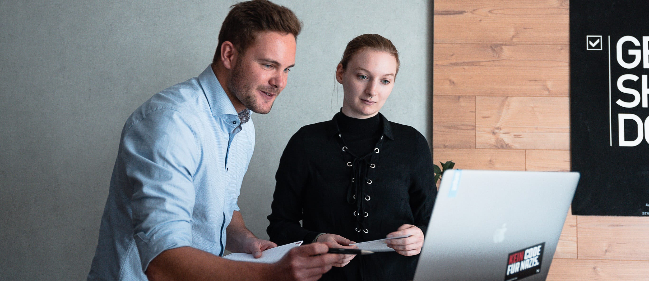 Laura Burchert und Jonas Ludwig stehen vor einem Laptop und analysieren in einem internen Forschungsprojekt den Bewerbungsablauf bei enpit.